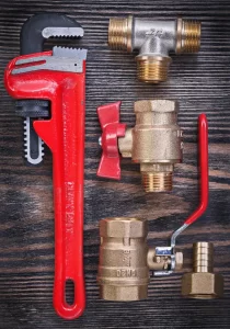 Plumbing wrench and brass pipe fittings on wooden surface