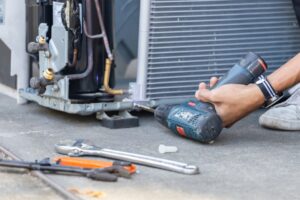 Technician repairing air conditioning unit with power drill